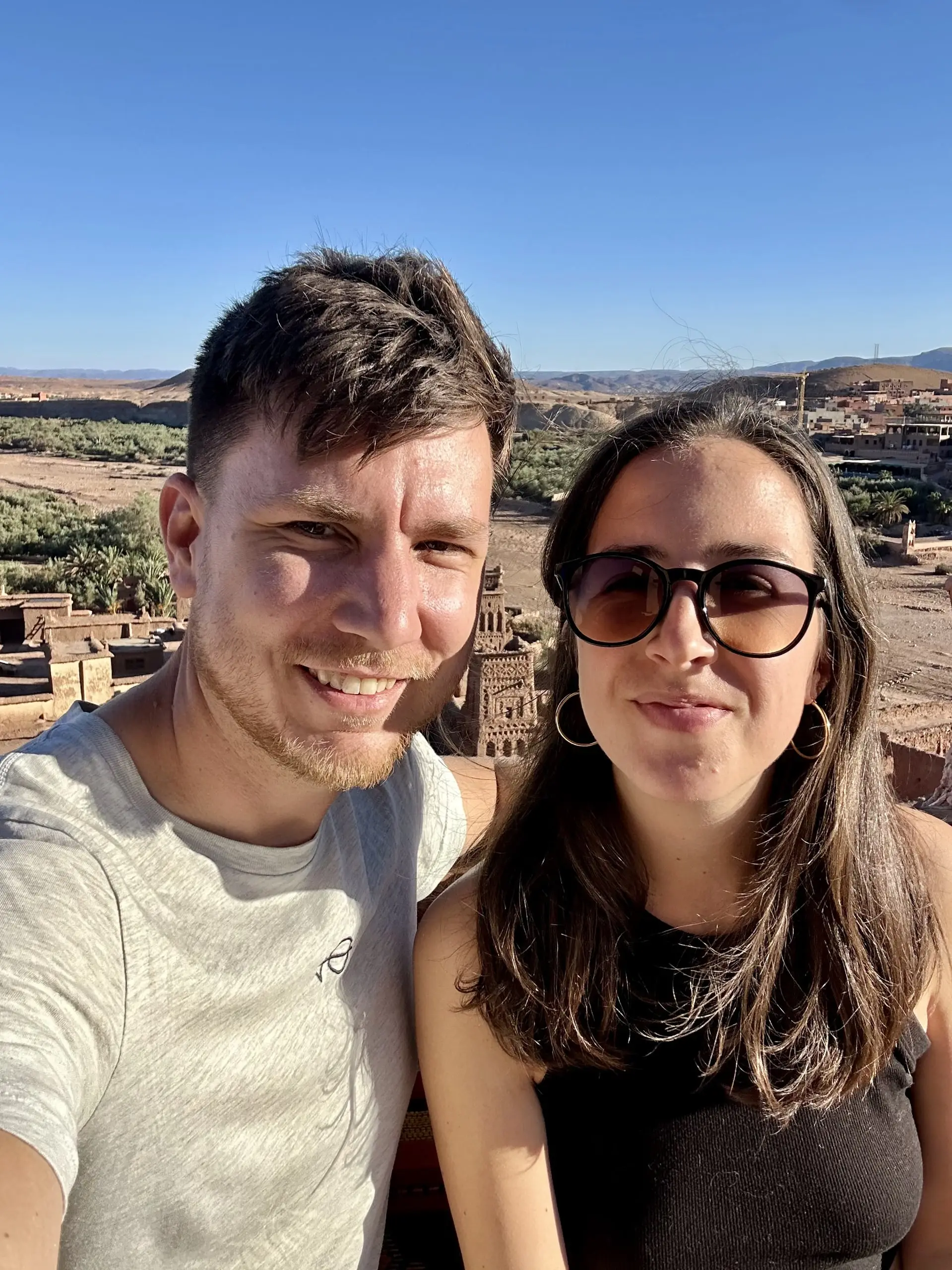 Naše selfie, oba se usmíváme, za námi se v údolí rýsuje hliněný ksar Aít Benhaddú.