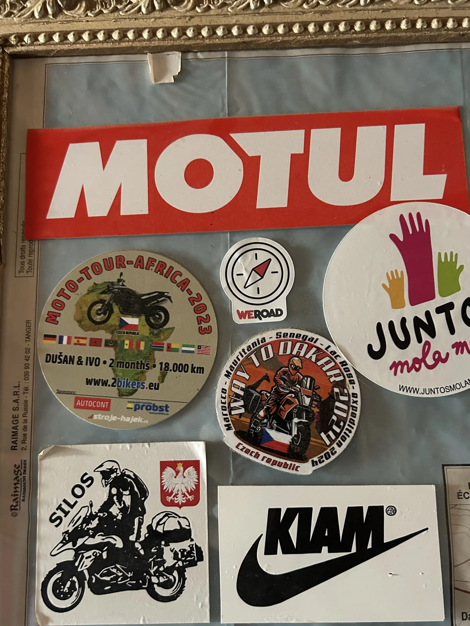 Nástěnka pokrytá motorkářskými a cestovatelskými samolepkami včetně velkého nápisu Motul a Way to Dakar.
