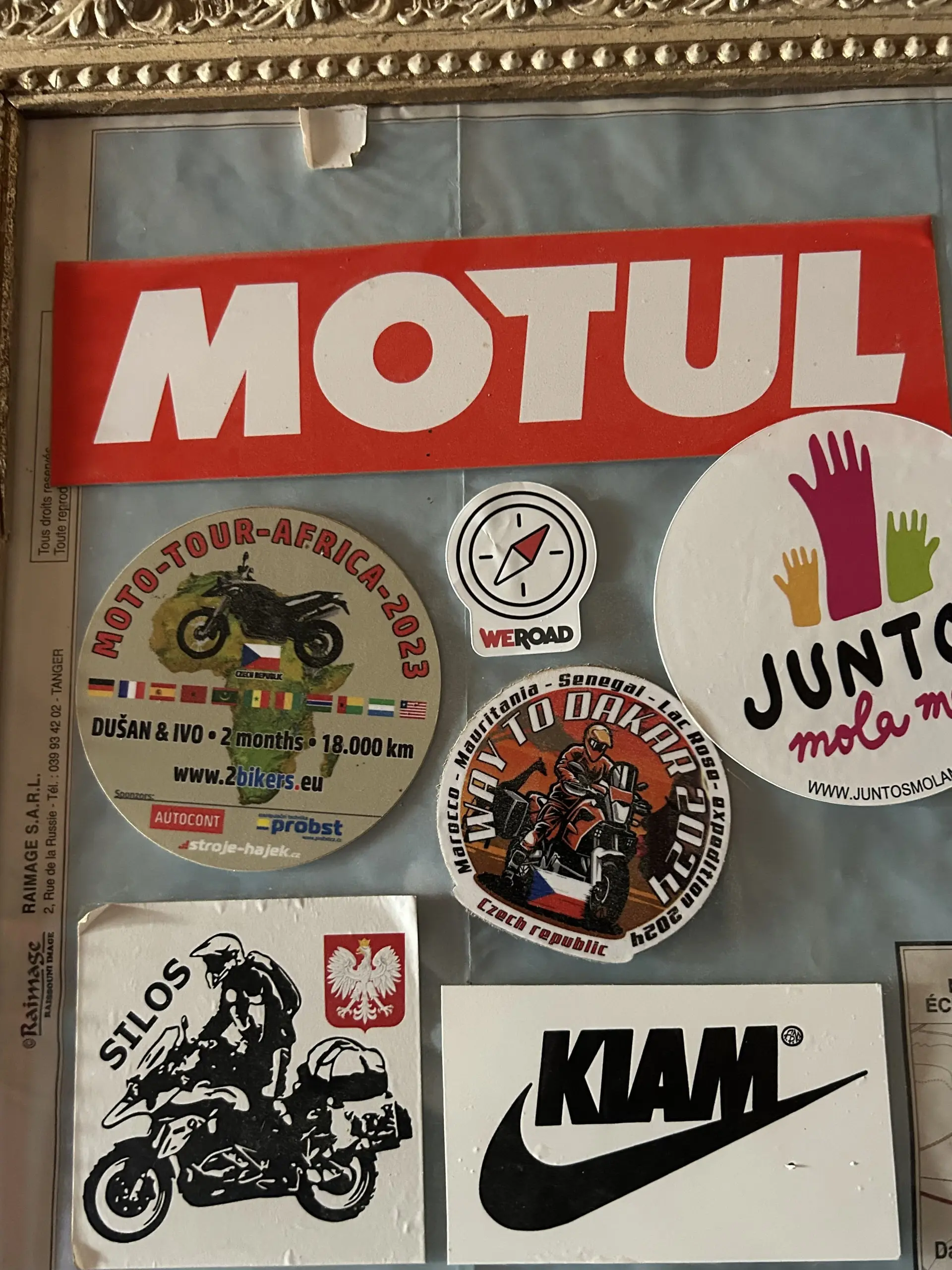 Nástěnka pokrytá motorkářskými a cestovatelskými samolepkami včetně velkého nápisu Motul a Way to Dakar.