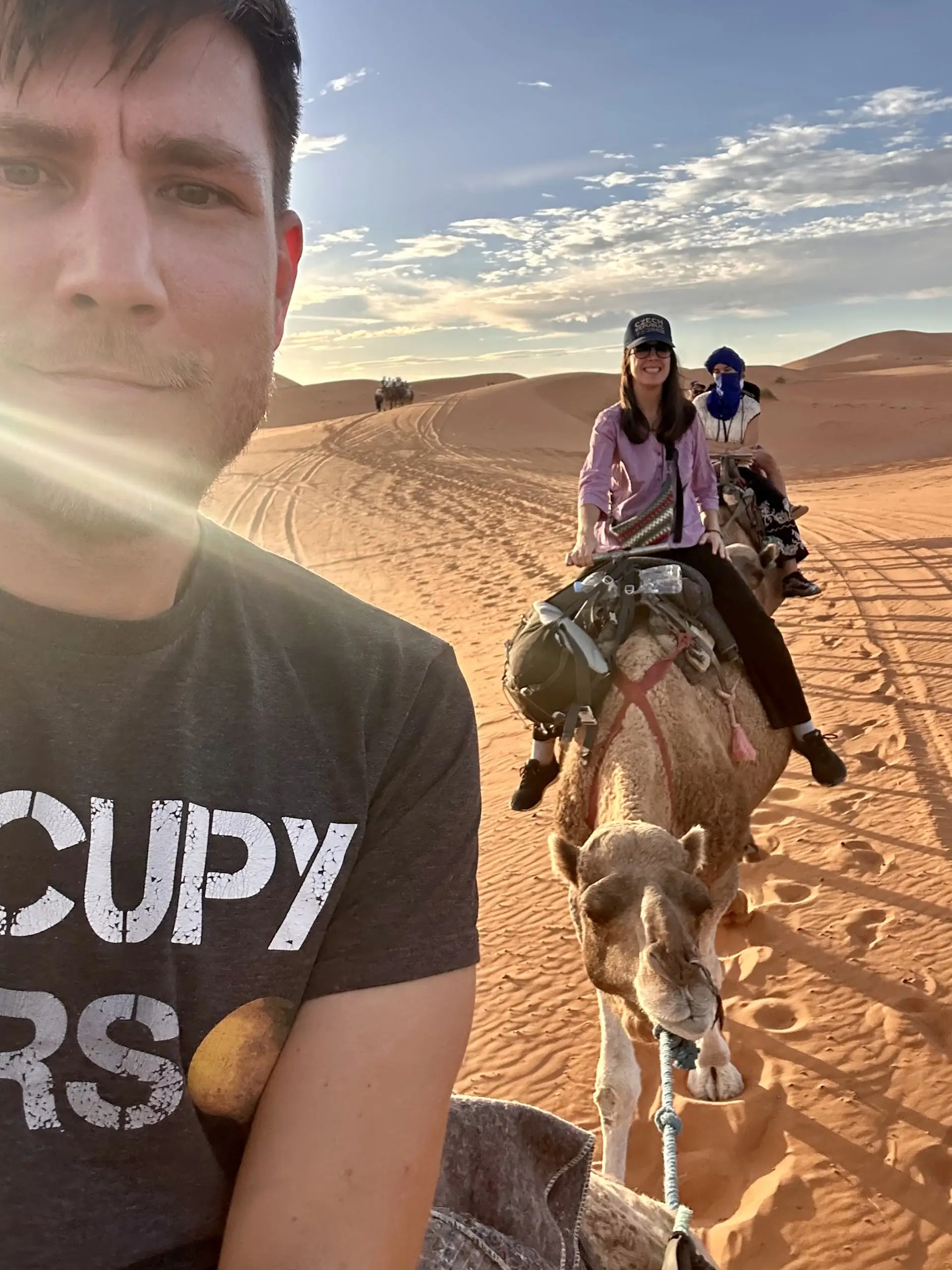 Selfie, v popředí já, za mnou Anička na velbloudovi a berberský vůdce, kolem zlaté duny v podvečerním slunci.