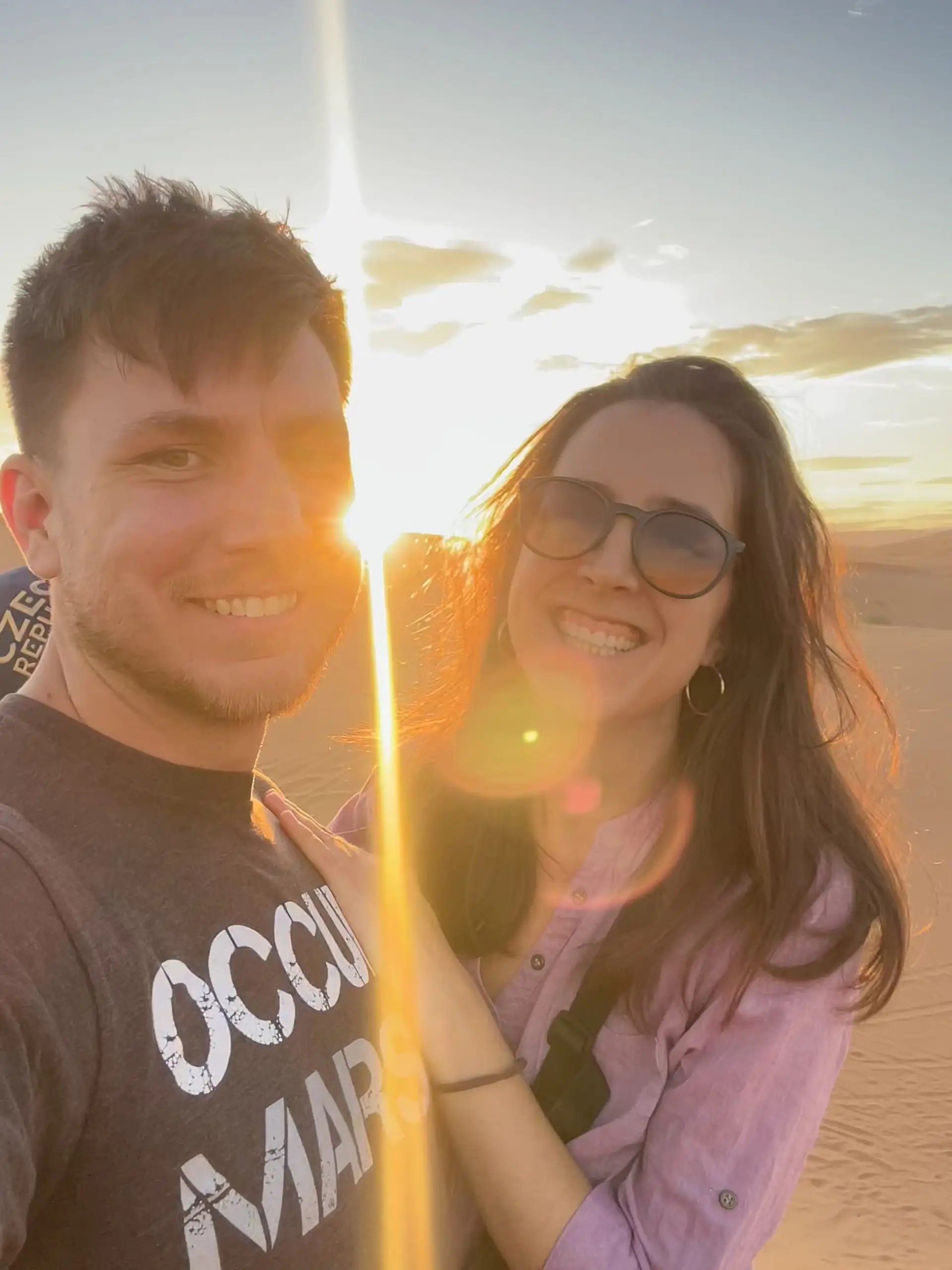 Usmíváme se s Aničkou do selfie na duně, mezi námi prosvítá zapadající slunce.