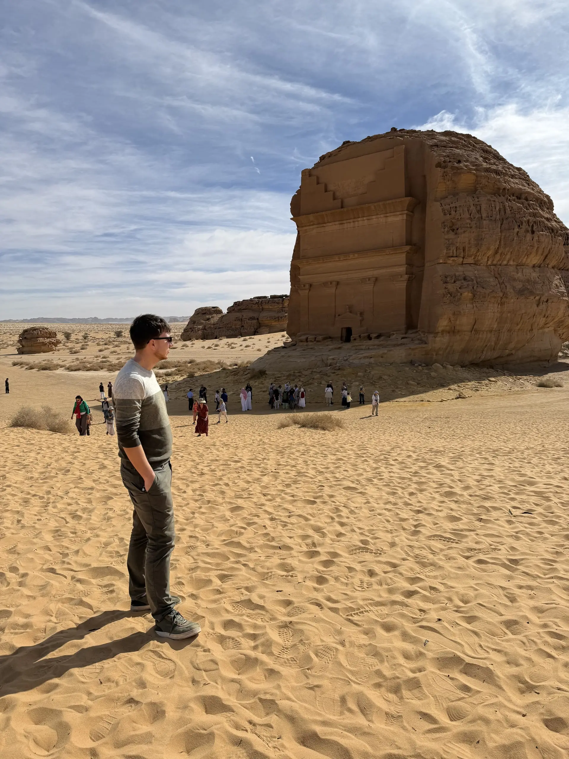 Jeden z nás stojí v písku a hledí na osamělou nabatejskou hrobku Qasr al-Farid s davem turistů pod ní.