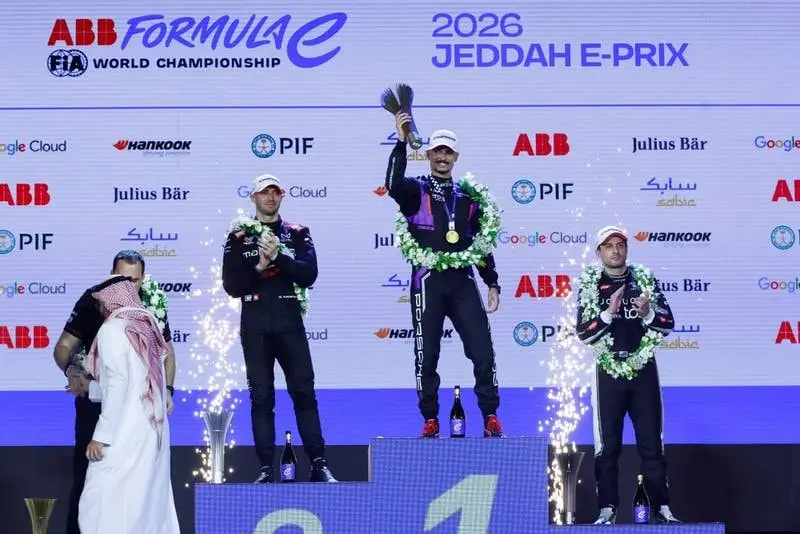 Tři jezdci s věnci na stupních vítězů pod nápisem 2026 Jeddah E-Prix, vítěz zvedá trofej a kolem šlehají ohňostroje.