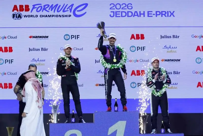 Tři jezdci s věnci na stupních vítězů pod nápisem 2026 Jeddah E-Prix, vítěz zvedá trofej a kolem šlehají ohňostroje.