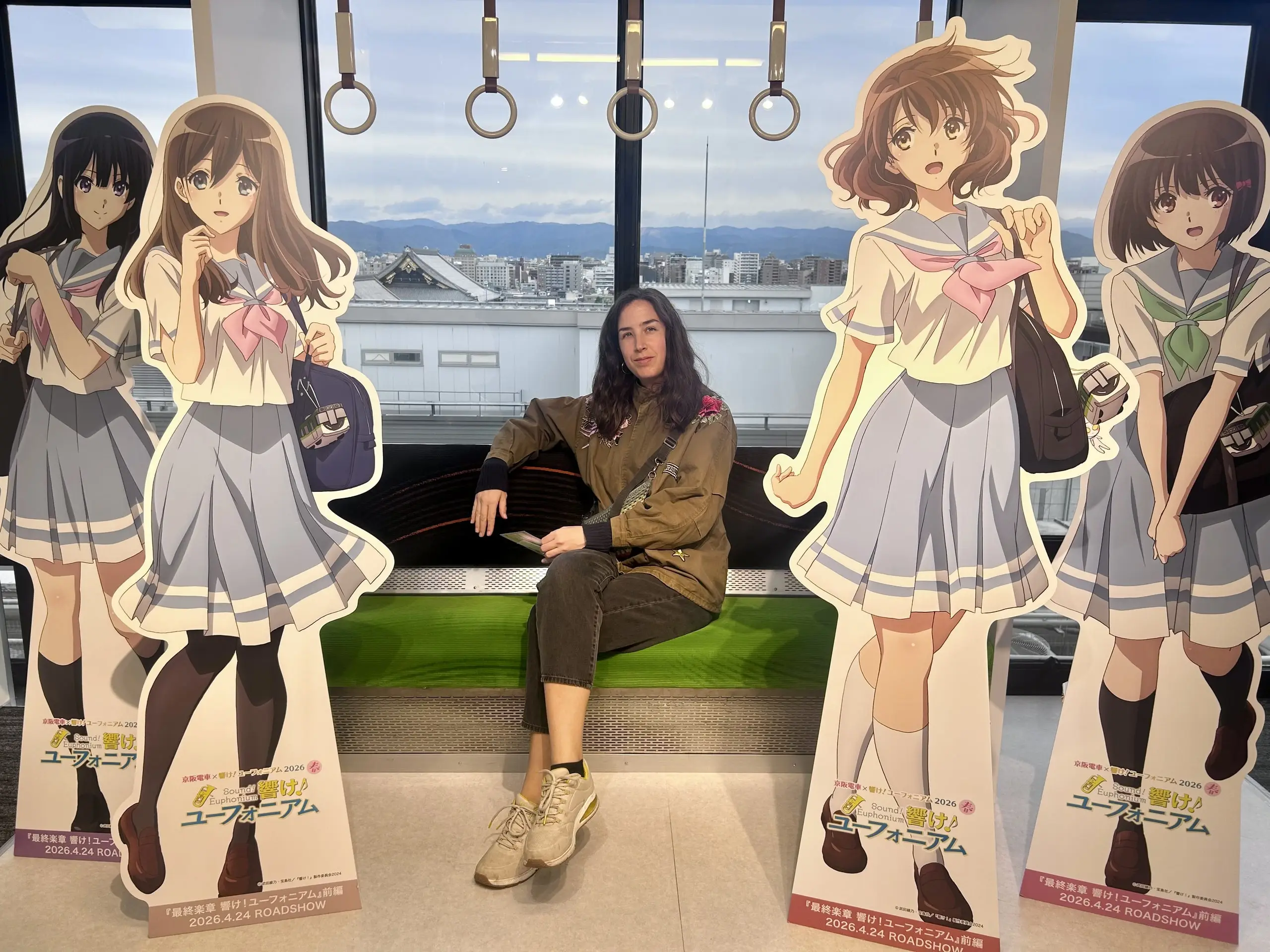 Žena sedí na zelené lavici mezi velkými stojanovými figurínami dívek v japonských uniformách.