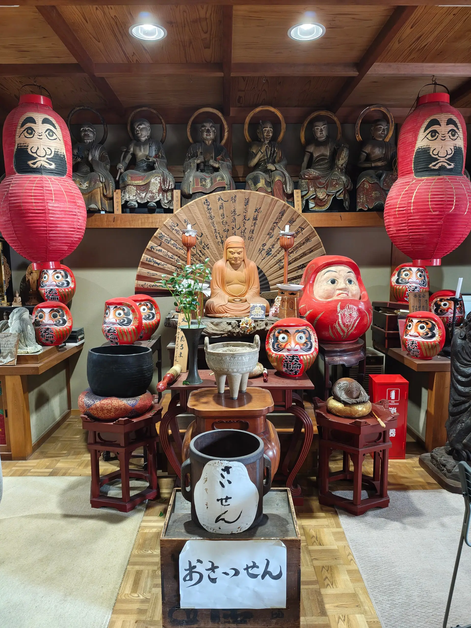 Vnitřní oltář Daruma svatyně s buddhistickými soškami, červenými lampiony a malovanými figurkami daruma.