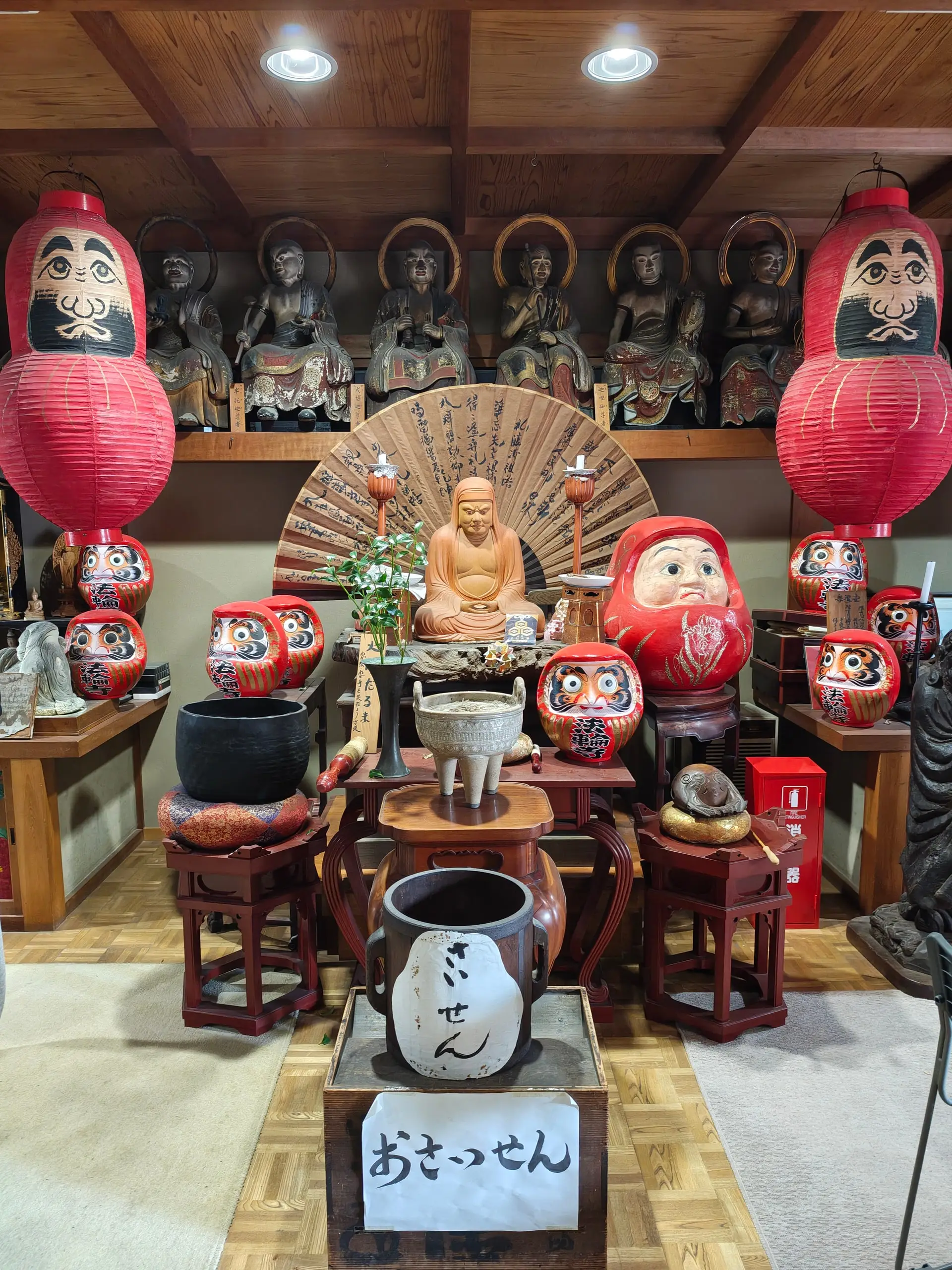 Vnitřní oltář Daruma svatyně s buddhistickými soškami, červenými lampiony a malovanými figurkami daruma.