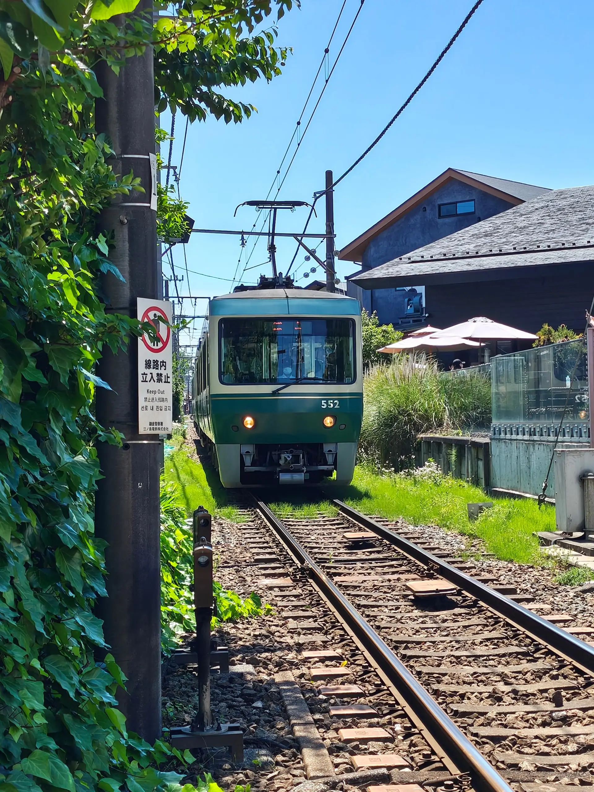 Zelenobílá tramvaj Enoden přijíždí po kolejích vedoucích mezi domy a zelení.