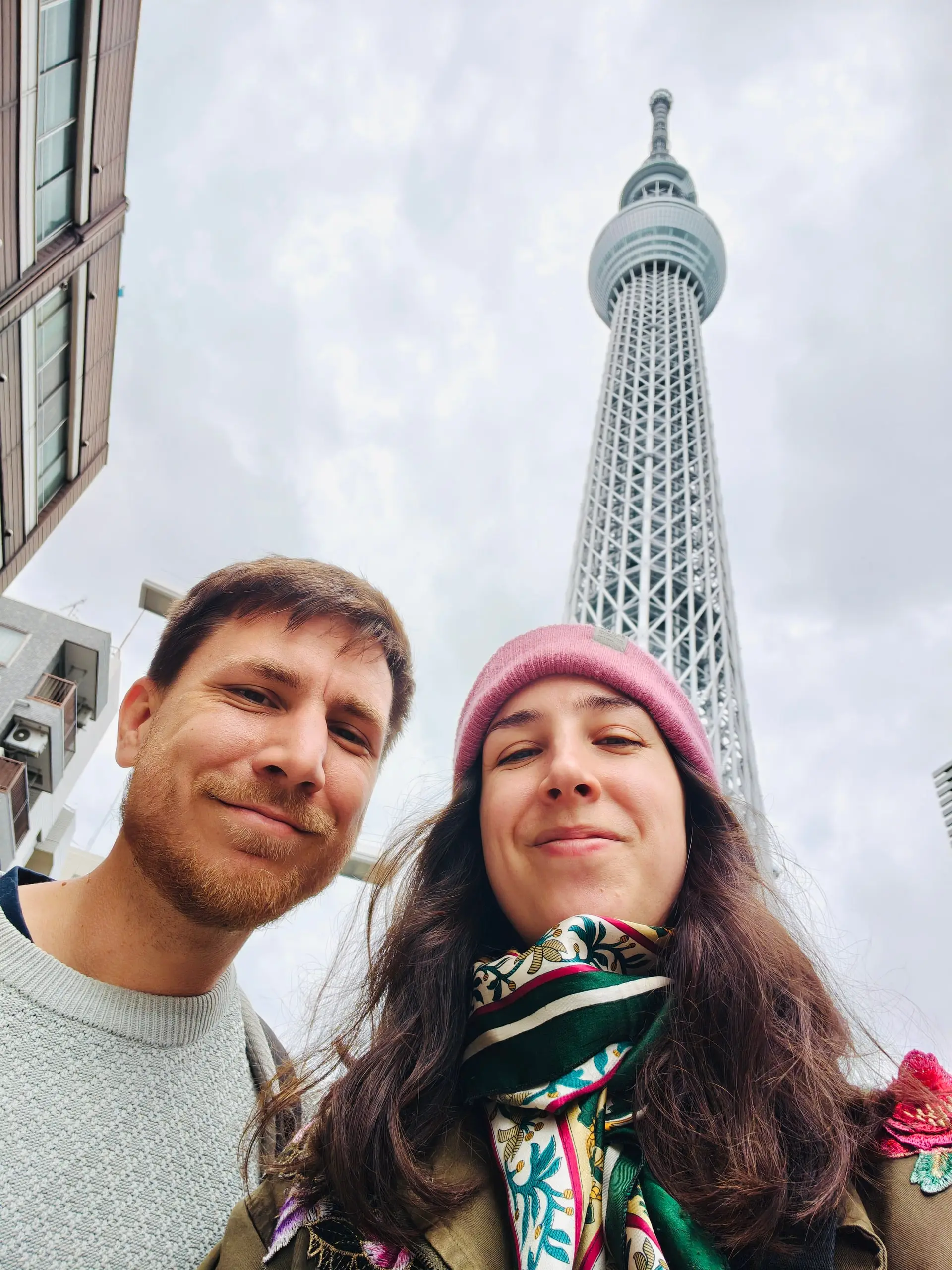 Dvojice se fotí pod věží Tokyo Skytree pod zataženou oblohou.