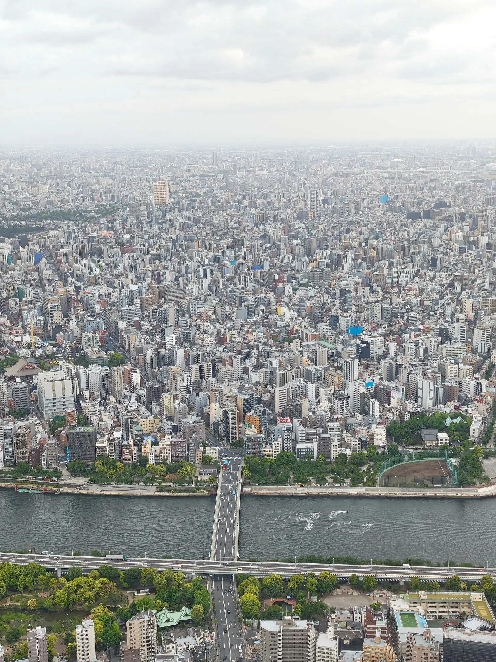 Letecký pohled z věže Skytree na hustou zástavbu Tokia s řekou a mostem.