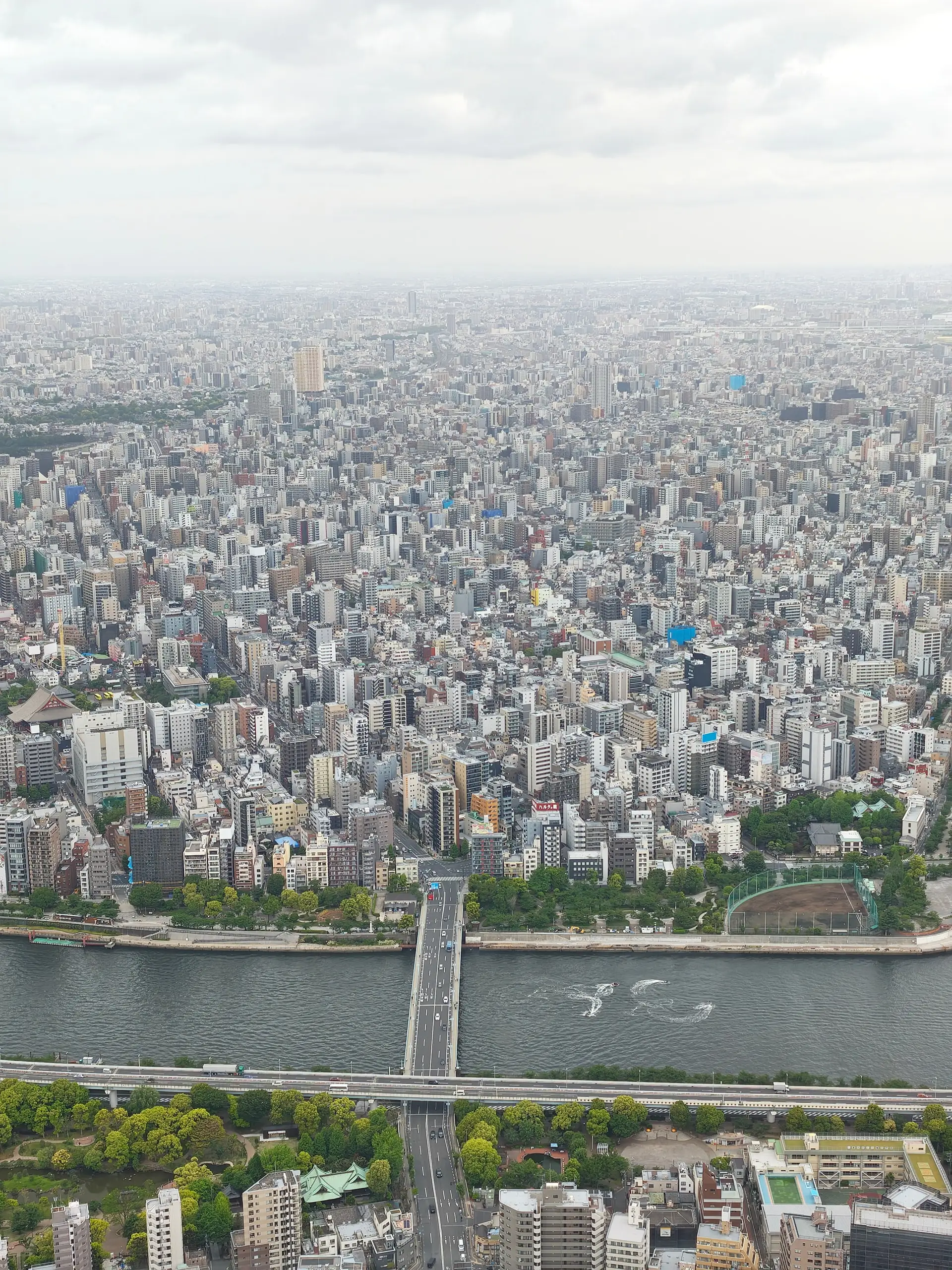 Letecký pohled z věže Skytree na hustou zástavbu Tokia s řekou a mostem.