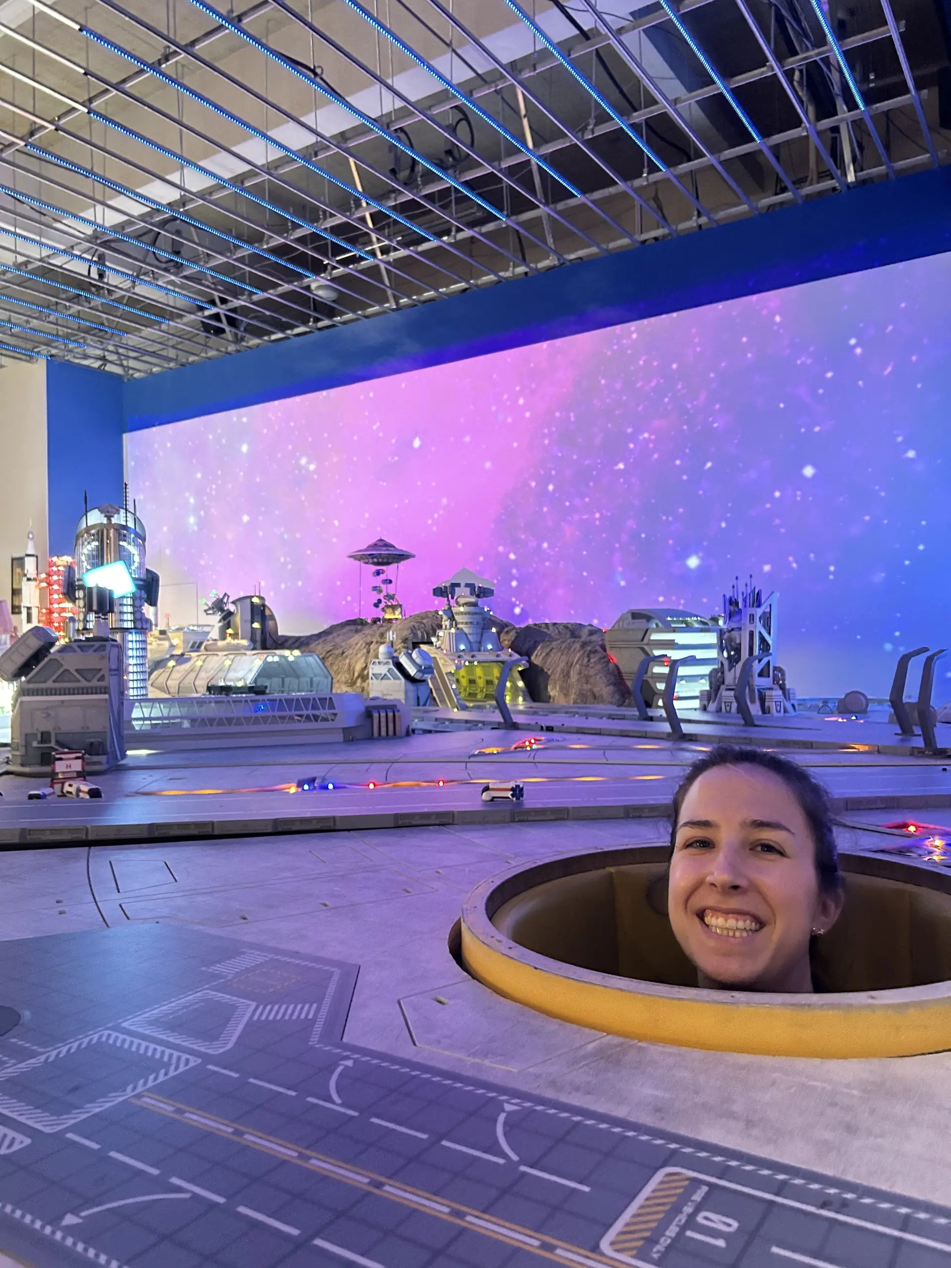 Anička vykukuje z otvoru v interaktivní vesmírné scéně s planetární základnou na výstavě Small Worlds.