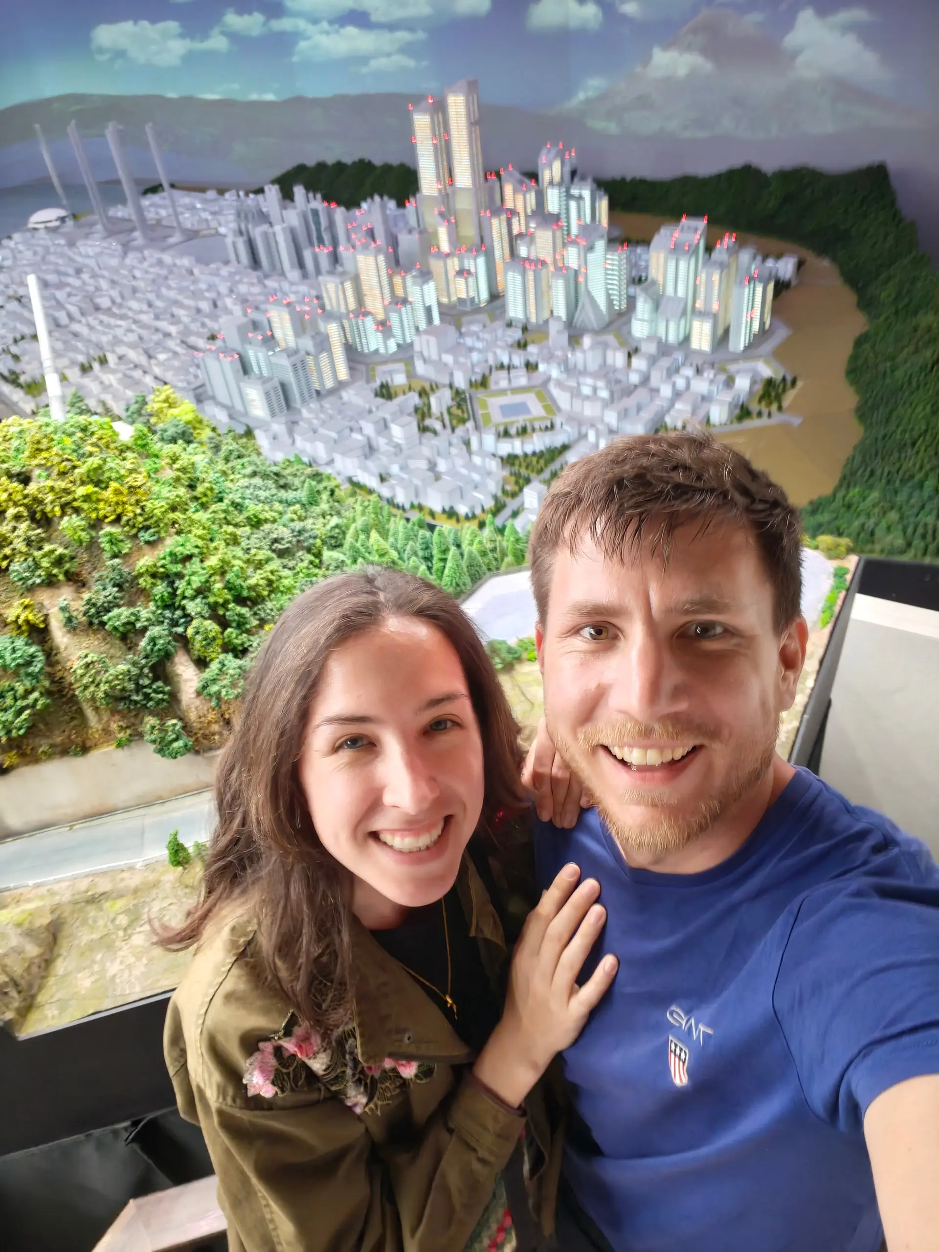 Dvojice se usmívá před velkým miniaturním modelem moderního města na výstavě Small Worlds.