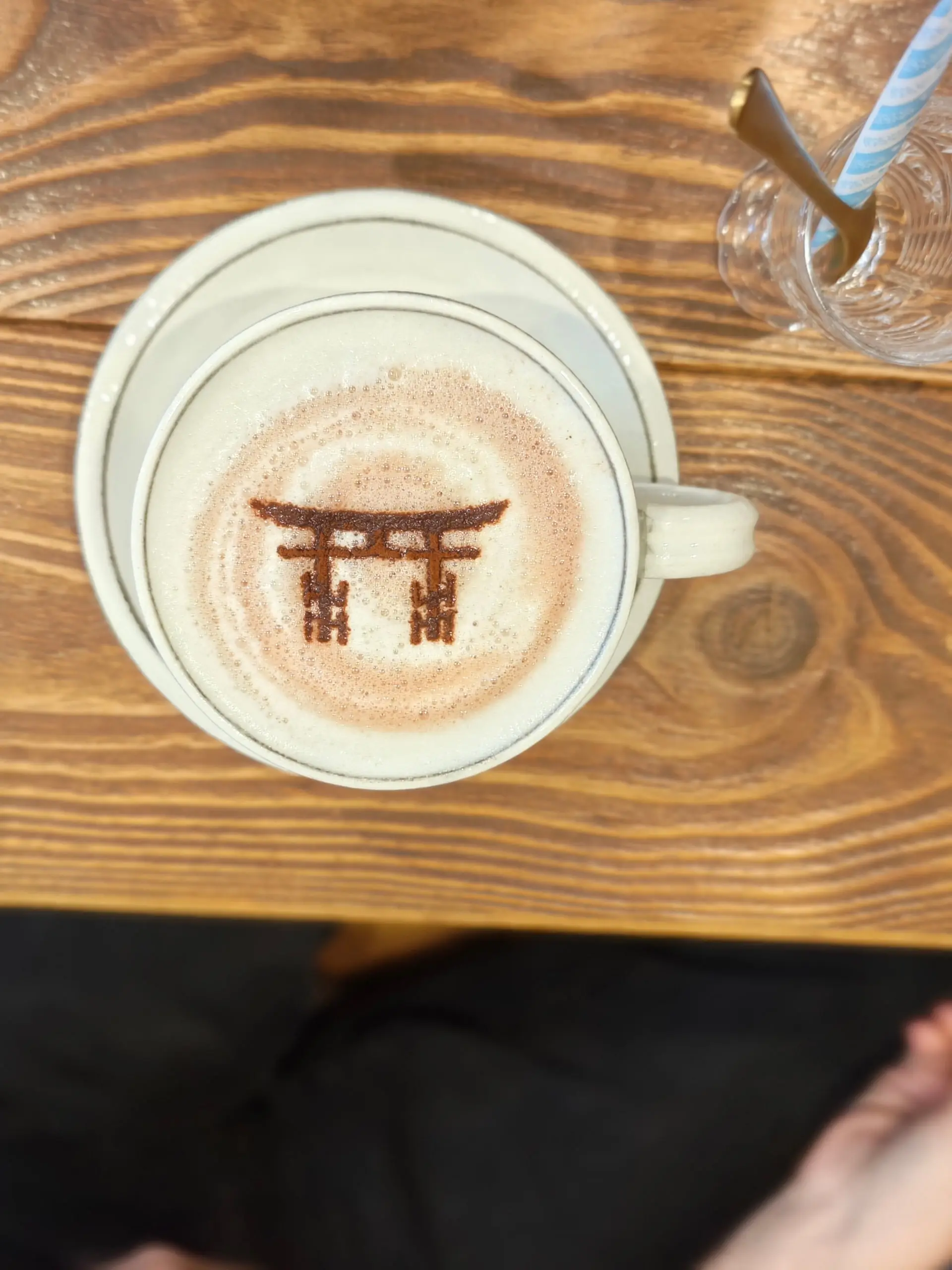 Šálek kávy latte se zákresem brány torii v mléčné pěně na dřevěném stole.